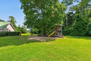 A playground with a slide and a swing set, surrounded by a well-maintained lawn and trees. - Modern Tifton Getaway - 3BR + Pool Access (Tifton)