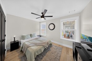 A bedroom with a bed, a nightstand, a ceiling fan, a clock, and a window with blinds. - Modern Tifton Getaway - 3BR + Pool Access (Tifton)