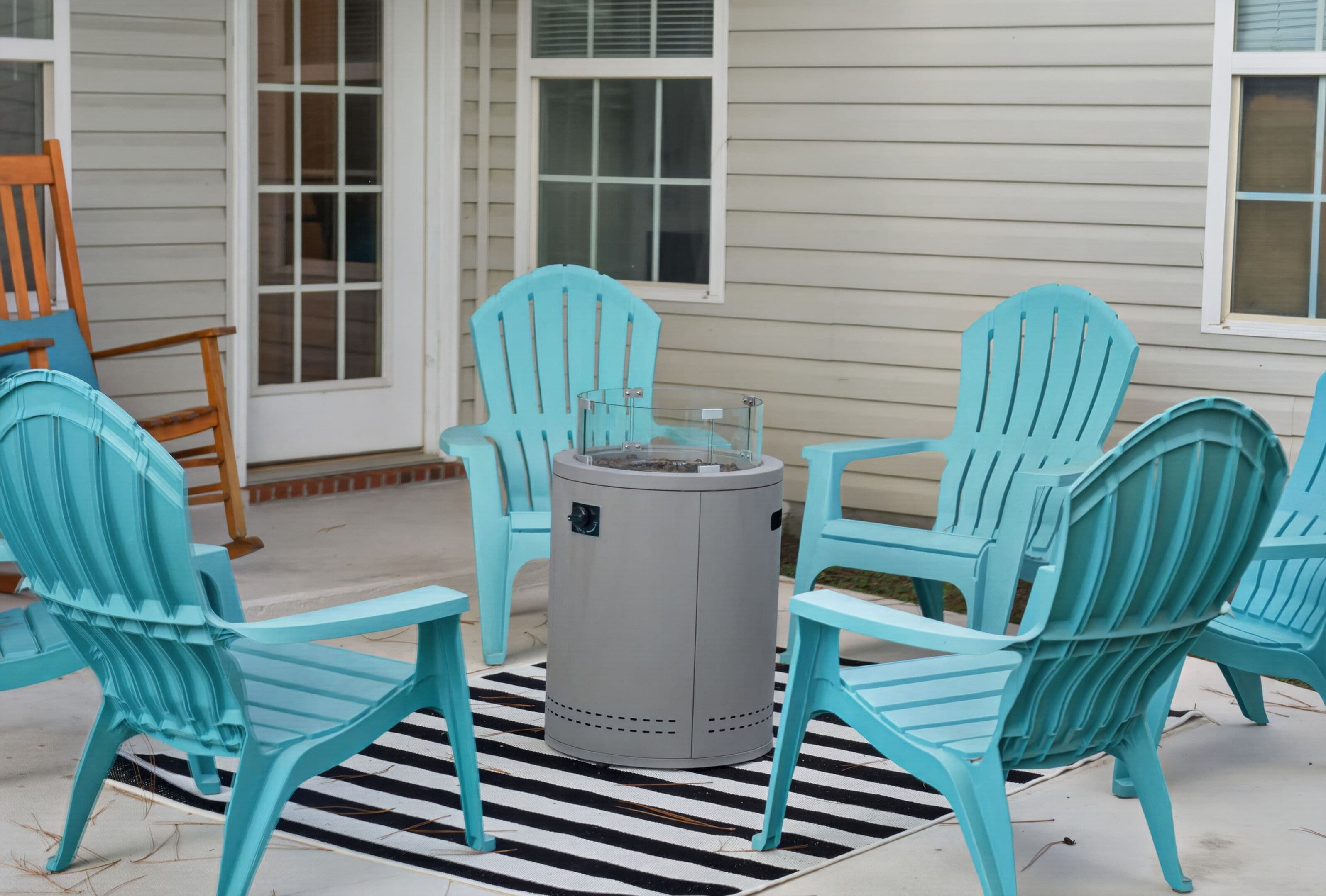 A patio with four turquoise Adirondack chairs arranged around a central gray fire pit.
