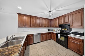 A modern kitchen with wooden cabinets, stainless steel appliances, and a white countertop. - Modern Tifton Getaway - 3BR + Pool Access (Tifton)