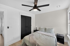 A bedroom with a bed, a nightstand, a bedside table, a ceiling fan, and a door. - Modern Tifton Getaway - 3BR + Pool Access (Tifton)