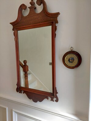 A wall-mounted mirror with an ornate frame, a small round clock, and a reflection of a staircase.