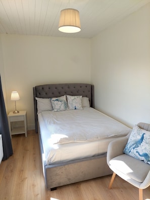 A bedroom with a bed, a nightstand, a chair, and a hanging light fixture.
