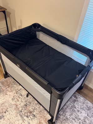 A portable crib with a mesh side and a solid black mattress, placed on a patterned rug. - Cozy corner in The Burgh, Minutes to Downtown (Pittsburgh)