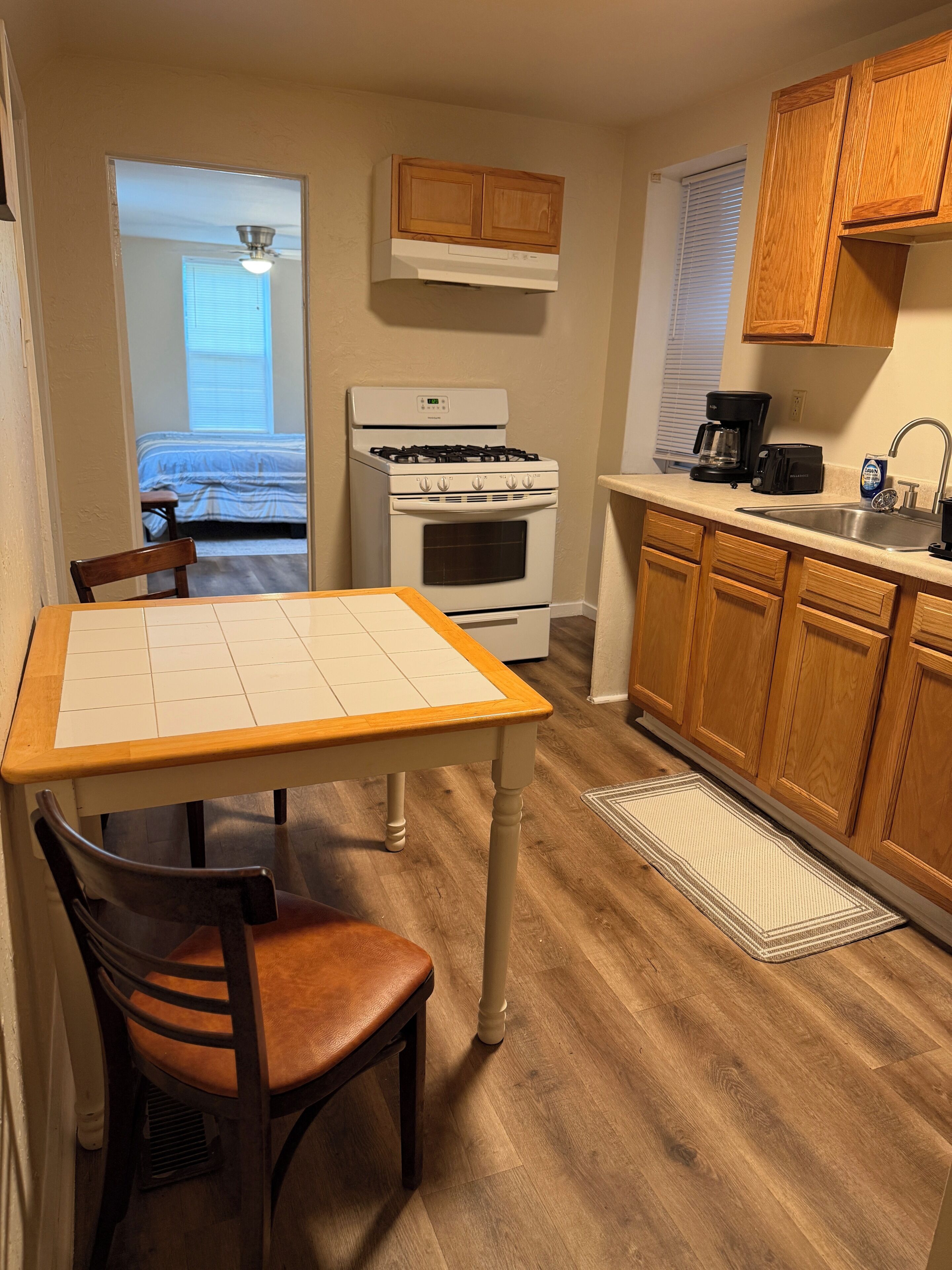 A compact kitchen with a dining table, wooden cabinets, a stove, and a coffee maker.