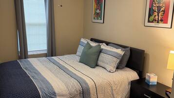 A bedroom with a bed, a nightstand, a drawer unit, a ceiling fan, and two wall art pieces.
