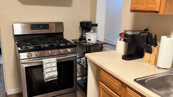 A kitchen with a stainless steel stove, an oven, wooden cabinets, a window with blinds, and a countertop with a coffee maker and utensils.