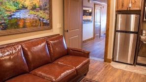 Ein braunes Ledersofa in einem Raum mit Holzboden, einem Edelstahlkühlschrank und einem Gemälde einer Flusslandschaft an der Wand.