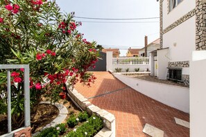 A narrow paved pathway flanked by a white wall and a building with a stone facade.