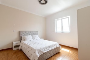 A bedroom with a bed, a nightstand, a window, and a wooden floor.
