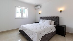 A bedroom with a bed, a nightstand, a window, and an air conditioning unit. - Spacious 5-Bedroom Villa with Garden Near Lisbon ,Sesimbra& beautiful beaches (Quinta Do Conde)