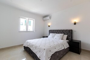 A bedroom with a bed, a nightstand, a window, and an air conditioning unit. - Spacious 5-Bedroom Villa with Garden Near Lisbon ,Sesimbra& beautiful beaches (Quinta Do Conde)