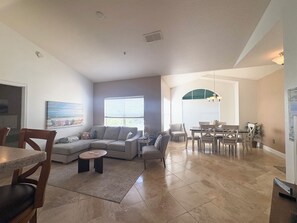 A spacious living room with a sectional sofa, a dining area with a table and chairs, and a kitchen area with a refrigerator.