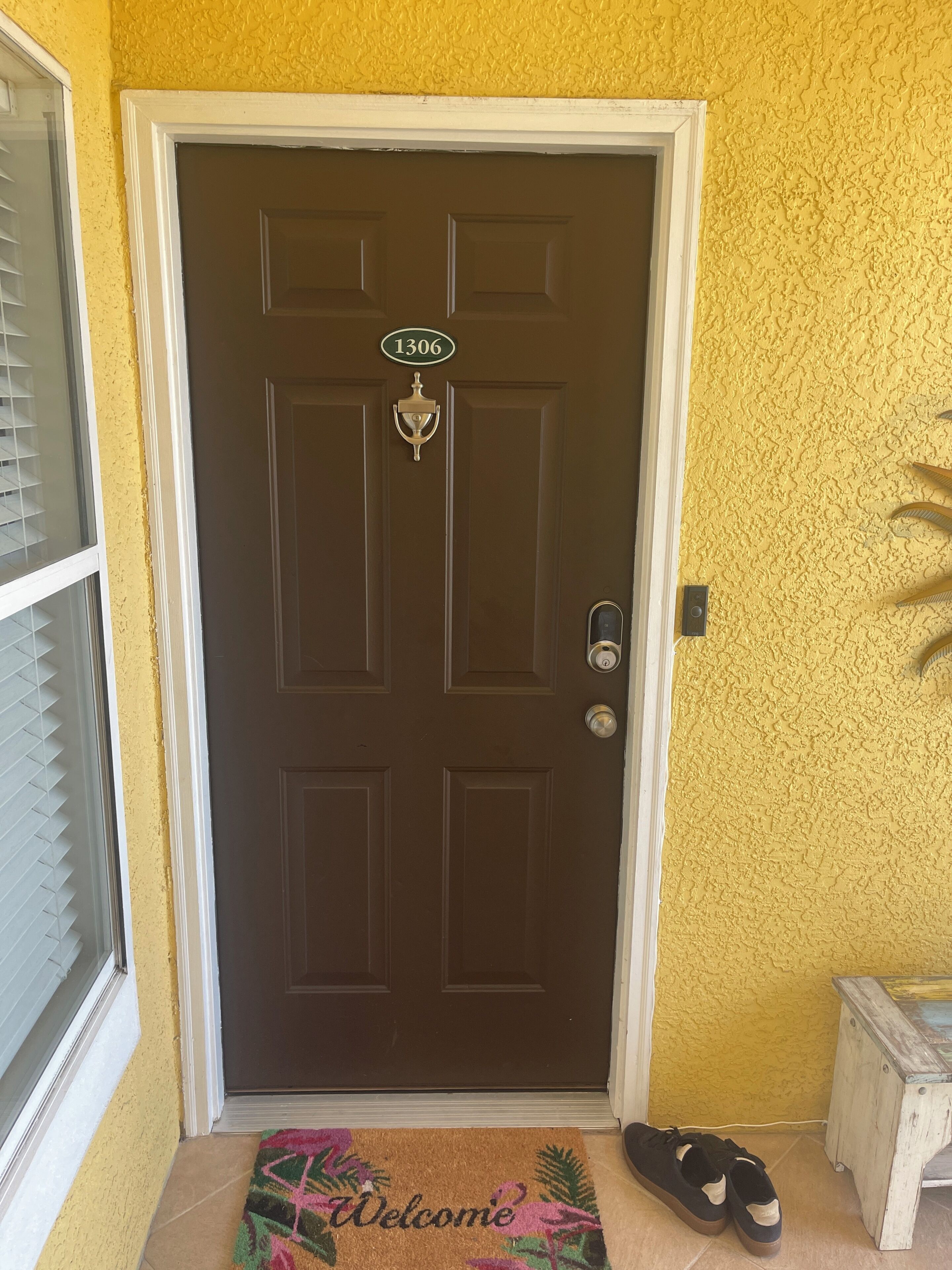 A brown door with a number plate, a doormat, and a pair of shoes on the ground.