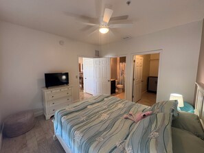 A bedroom with a bed, a television on a dresser, a ceiling fan, and a bathroom visible through an open door.