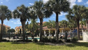 A pool area surrounded by palm trees and a fence, with buildings in the background. - Two Bed Two Bath Seminole Stay (Seminole)