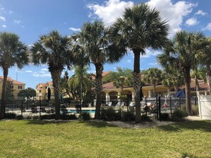 A pool area surrounded by palm trees and a fence, with buildings in the background. - Two Bed Two Bath Seminole Stay (Seminole)
