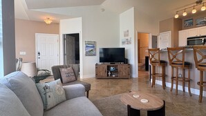 A living room with a sofa, a coffee table, a TV, and a kitchen area with bar stools. - Two Bed Two Bath Seminole Stay (Seminole)