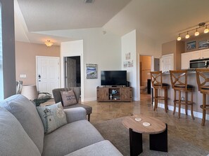A living room with a sofa, a coffee table, a TV, and a kitchen area with bar stools. - Two Bed Two Bath Seminole Stay (Seminole)