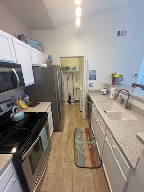 A kitchen with a stove, microwave, refrigerator, and a countertop with a blender and a vase of flowers. - Two Bed Two Bath Seminole Stay (Seminole)