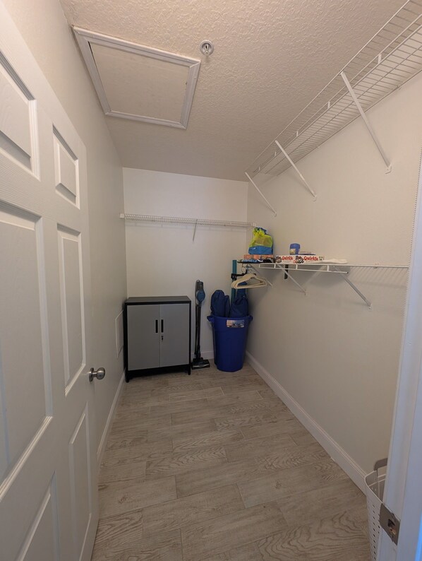 A laundry room with a cabinet, a vacuum cleaner, and shelves with cleaning supplies.