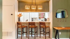 Uma cozinha com área de bar, armários brancos, luminária pendente e um espelho na parede.