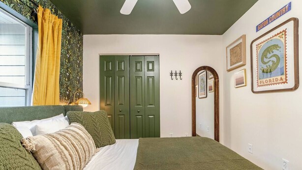 Quarto com cama, cortinas verdes, janela, porta e decoração nas paredes, incluindo uma placa com a palavra 'Florida'.