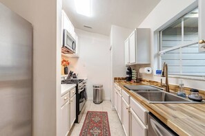 Eine kleine Küche mit weißen Schränken, einer Edelstahl-Spüle und einem Fenster, das für natürliches Licht sorgt.