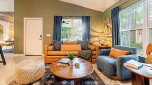 Uma sala de estar com sofá, poltronas, mesa de centro e um espaço de jantar com mesa e cadeiras.