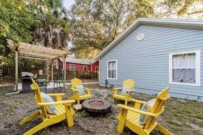 A backyard with a blue house, yellow Adirondack chairs, a wooden pergola, and a fire pit. - The Designer Boutique • 3BR/2BA by UF • Firepit (Gainesville)