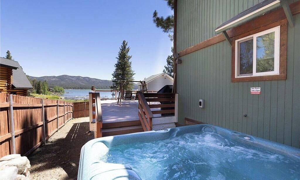 A hot tub with a wooden deck leading to a cabin by a lake.