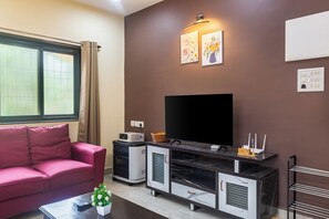 Uma sala de estar moderna com um sofá, uma televisão de tela plana, uma mesa de centro com uma planta e um armário com micro-ondas.