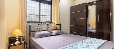 Un dormitorio con cama, mesita de noche, lámpara, ventana con cortinas y armario.