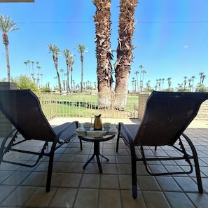 Eine Terrasse mit zwei Stühlen und einem Tisch, mit Blick auf Palmen und einen klaren Himmel.