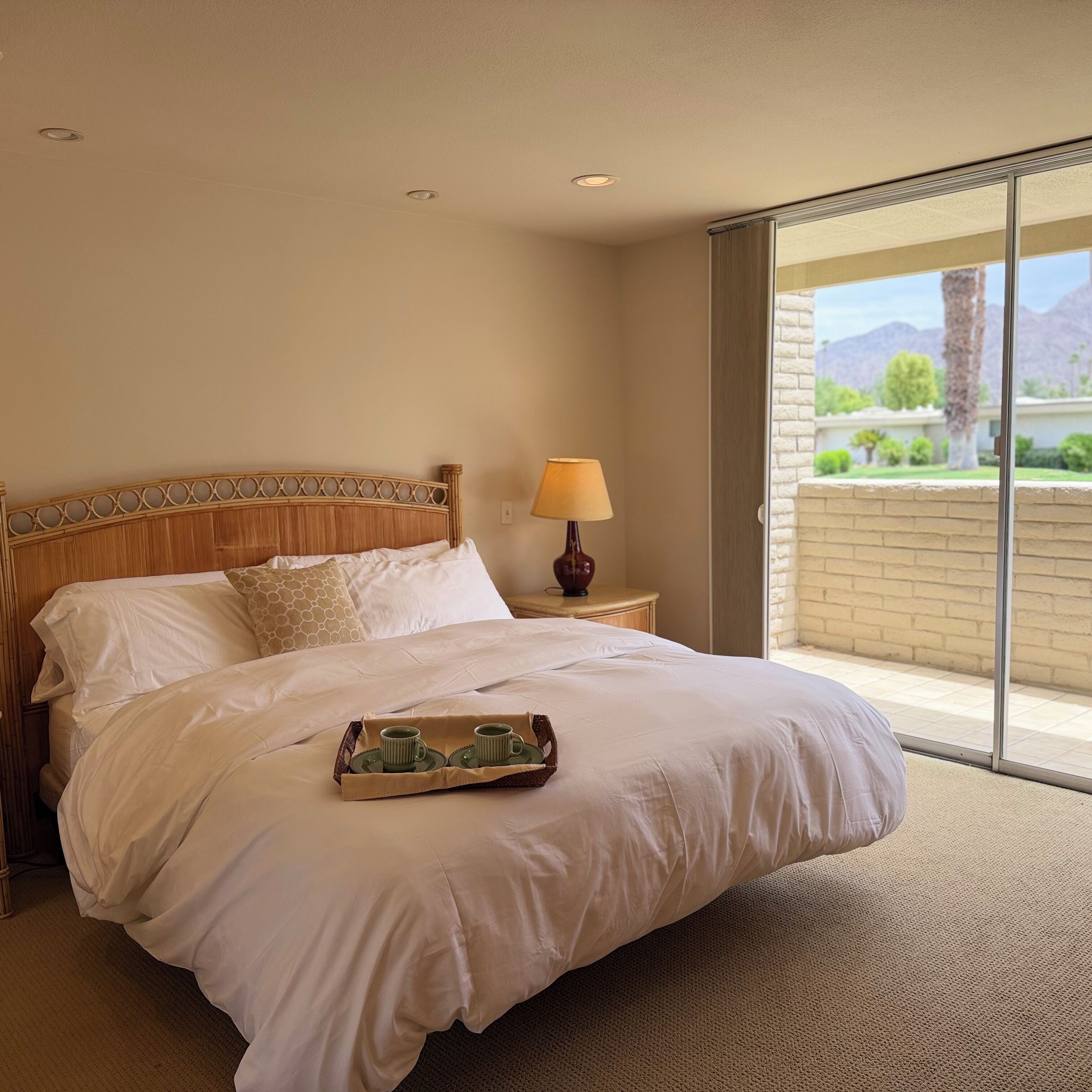 A hotel room with a large bed, a bedside table with a lamp, and a view of the outdoors.