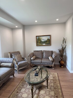 Ein Wohnzimmer mit zwei Sofas, einem Glastisch und einem Gemälde an der Wand.