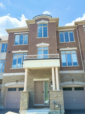 A multi-story residential building with a symmetrical facade, large windows, and a central entrance with a door and a small porch. - Great townhome in a family-friendly neighborhood (Ajax)