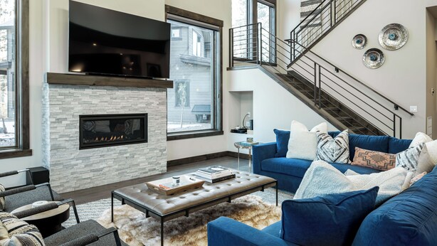 A modern living room with a stone fireplace, a blue sofa, and a staircase. - Sleek Mountain-Modern Townhome, Tucked in a Private Truckee Community (Truckee)