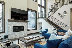 Una sala de estar moderna con una chimenea de piedra, un sofá azul y una escalera.