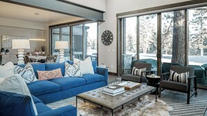 A spacious living room with a blue sofa, a coffee table, and a large window offering a view of trees. - Sleek Mountain-Modern Townhome, Tucked in a Private Truckee Community (Truckee)