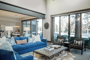 A spacious living room with a blue sofa, a coffee table, and a large window offering a view of trees. - Sleek Mountain-Modern Townhome, Tucked in a Private Truckee Community (Truckee)
