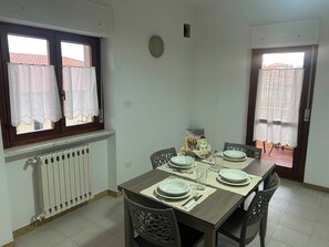 Une salle à manger avec une table dressée pour quatre personnes, un radiateur et une fenêtre avec des rideaux.