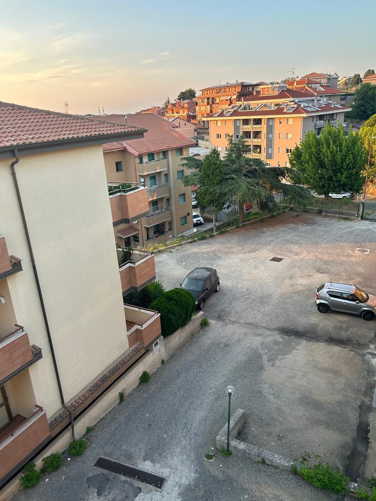Ein Wohngebiet mit Parkplatz, einem Gebäude mit beige-farbener Fassade und einer Reihe mehrstöckiger Wohngebäude im Hintergrund.