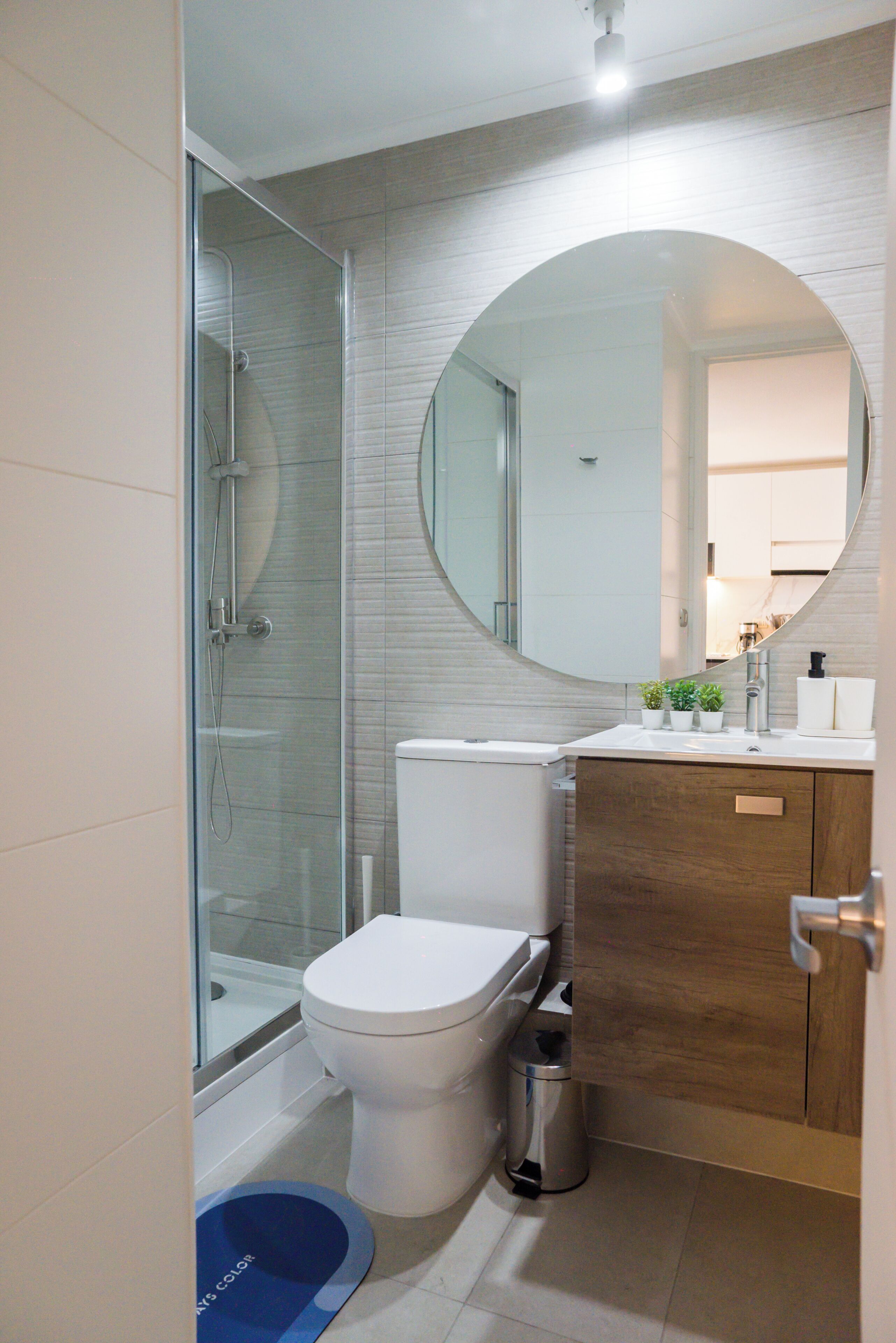 A modern bathroom with a glass shower enclosure, a toilet, a sink with a mirror, and a trash can.