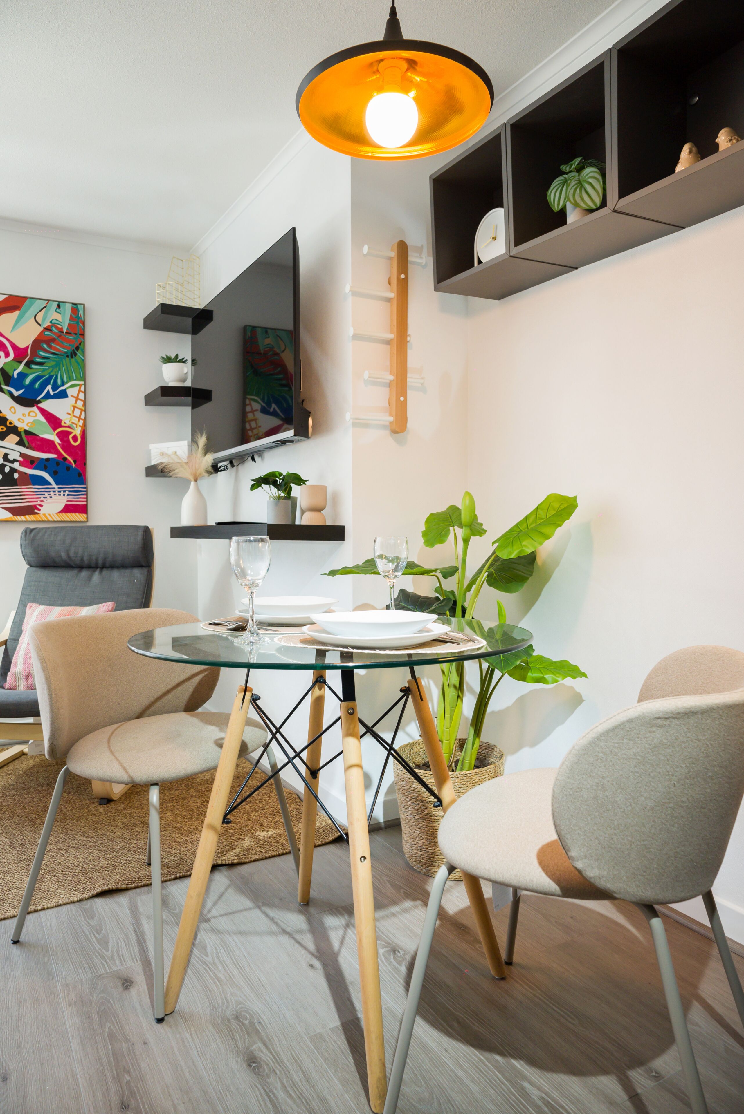 Uma área de refeições moderna com mesa de vidro, cadeiras de madeira e luminária pendente.