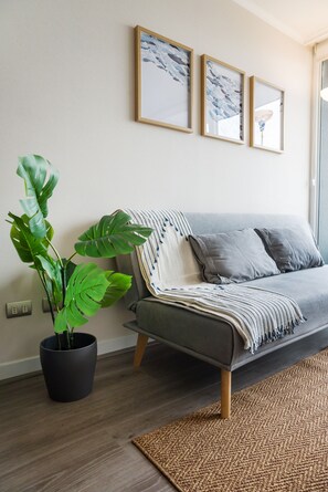 A modern living room with a grey sofa, a woven rug, and a large green plant. - Seminario Apartments by Andes STR (Ñuñoa)