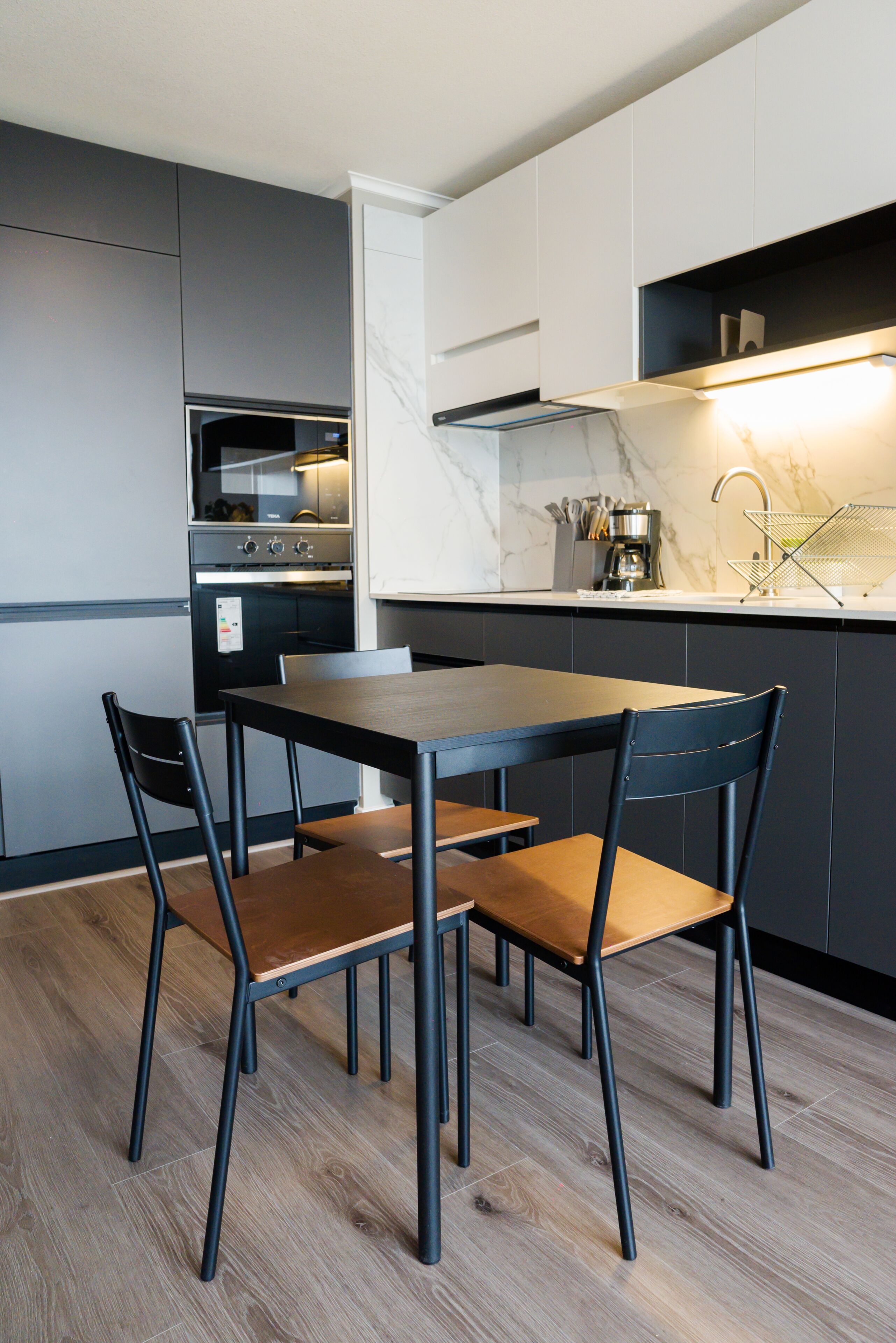 A modern kitchen with a dining table and chairs, a built-in oven, and a coffee machine.