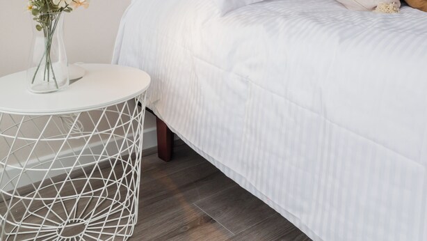 A neatly made bed with white bedding and a single pillow, a bedside table with a lamp and a vase of flowers, and a framed picture on the wall. - Seminario Apartments by Andes STR (Ñuñoa)