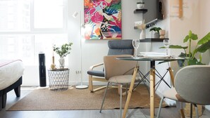 A modern living room with a dining area, a colorful abstract painting, and a large window. - Seminario Apartments by Andes STR (Ñuñoa)