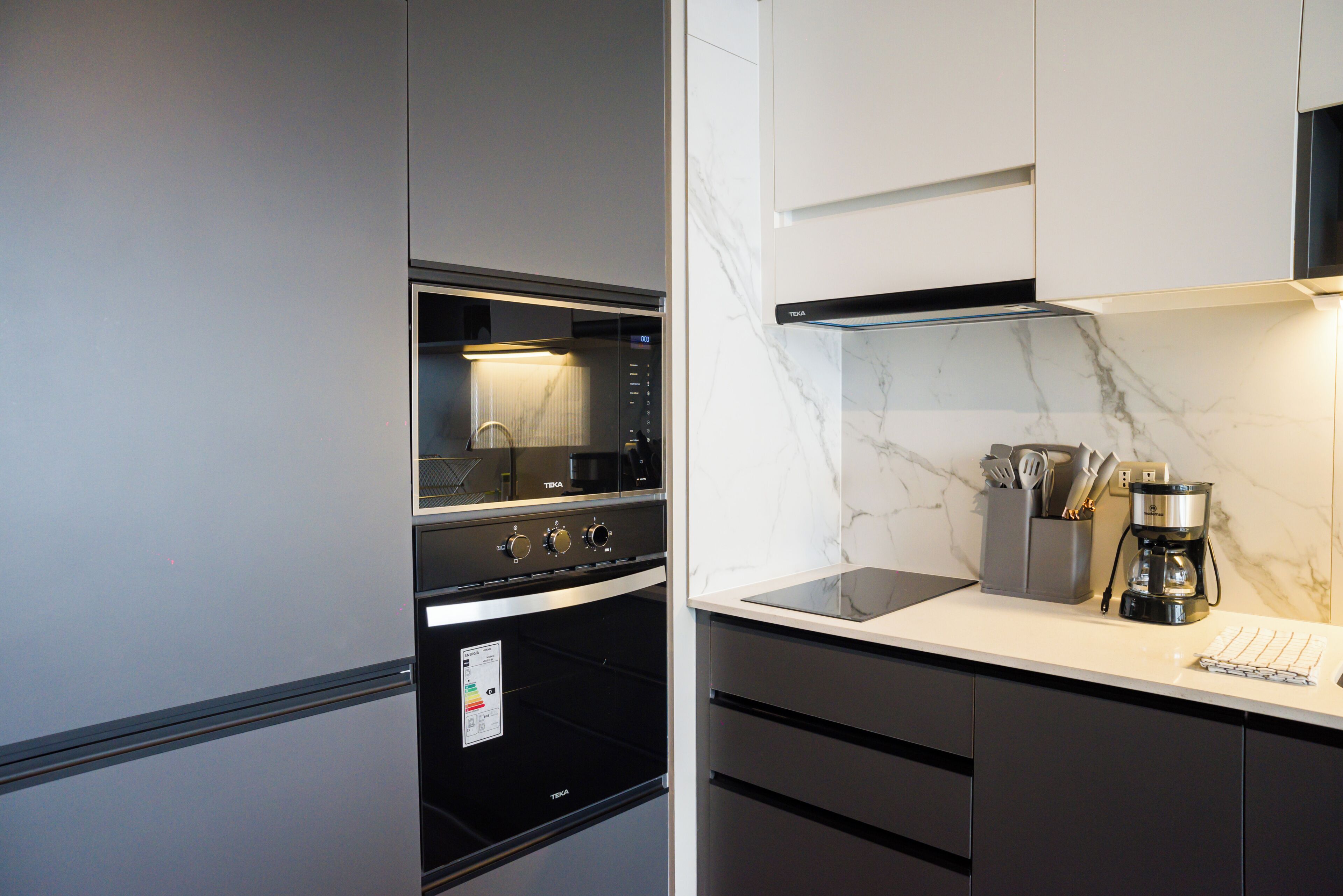 A modern kitchen with a built-in oven, a coffee maker, and a marble backsplash.